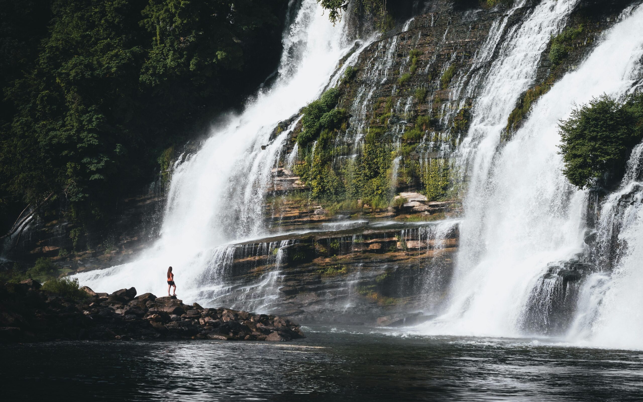 Woman stands on rock outcrop at base of Twin Falls, Rock Island, a grand double cascade waterfall. 